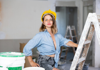 Portrait of tempting caucasian woman in revealing attire and helmet posing in construction site.