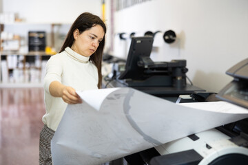 Attentive female employee of the printing house checks the quality of the print
