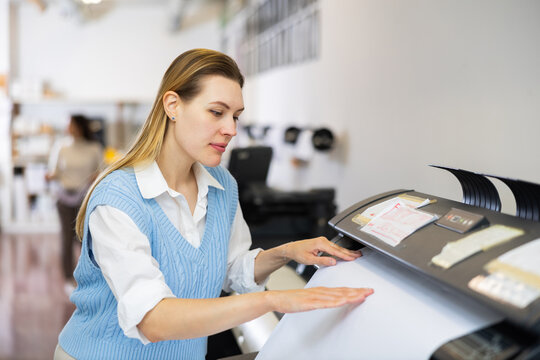 Woman working in publishing facility, loading large format paper in printer.