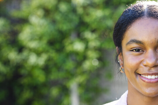 Young biracial woman smiles brightly outdoors, with copy space