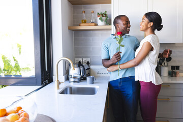 Young African American man surprises biracial woman with a rose at home