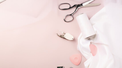 Tailoring accessories. White satin or silk fabric, scissors, chalk on pastel pink background. Woman hobby sewing