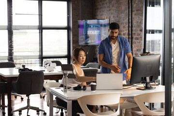 Young Asian man assists an Asian woman in a casual business office setting