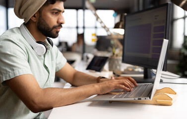 Young Asian man works diligently on a laptop in a casual business office setting