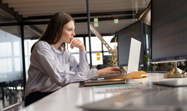 Fototapeta Young Caucasian woman works intently at her office desk in a casual business environment