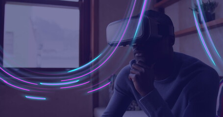 Image of glowing light trails of data transfer over african american man in vr headset