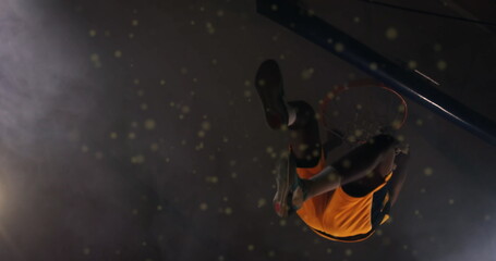 Image of particles moving over male basketball player scoring hoop