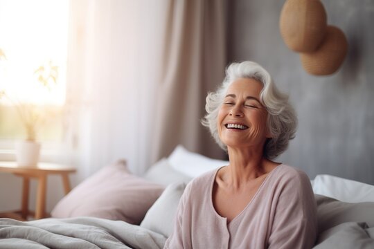 Happy Fresh Mature Middle Aged Woman Stretching In Bed Waking Up Alone Happy Concept, Smiling Old Senior Lady Awake After Healthy Sleep Sitting In Cozy Comfortable Bedroom Interior Enjoy Good Morning.