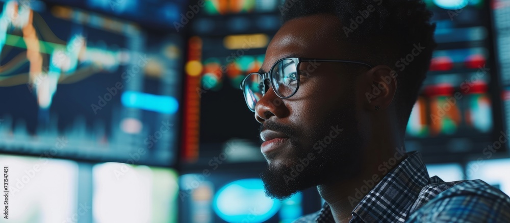 Wall mural a man with glasses is focused on a computer screen, surrounded by darkness and immersed in entertain