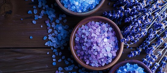Purple and blue dried lavenders accompany beauty product samples, resting on a dark wood table with bath salts.