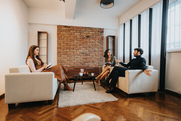 Three adults in a stylish living room, two conversing on a couch and one reading a notebook, casual and relaxed atmosphere. - obrazy, fototapety, plakaty