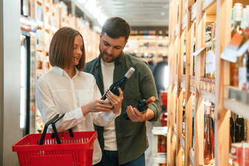 Holding the bottle. Man and woman are choosing wine in the shop