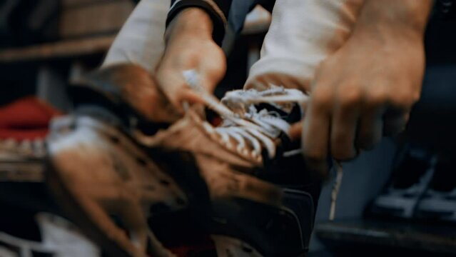 Ice hockey player ties the laces on his shabby, worn out skates in cloakroom before a game. Locker room indoor. Man get dressed and puts on his sports uniforms, tracksuit in dressing room. Close up
