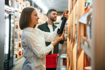 Side view. Man and woman are choosing wine in the shop