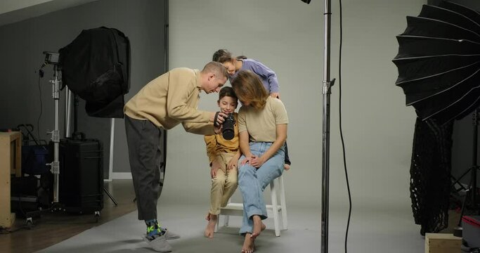 Family photo shooting. Photographer shows photos on camera. Happy family mom son daughter together in studio. Family album