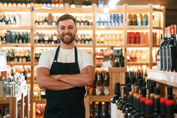 With arms crossed. Wine shop owner in white shirt and black apron
