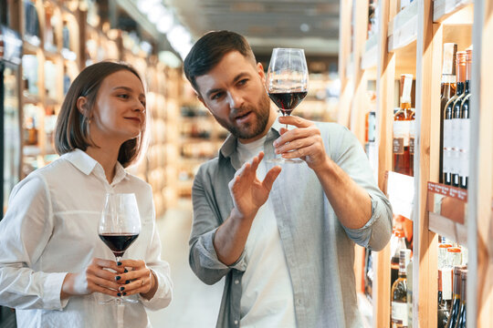 Glasses with drink. Take a sample. Man and woman are choosing wine in the shop