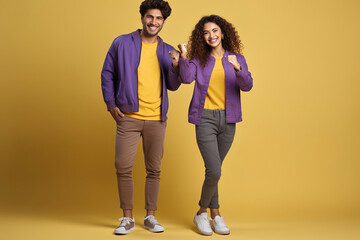 Happy excited couple holding fists while celebrating luck and lottery win. Excited friends wearing purple jackets, smiling at camera and standing over yellow background.