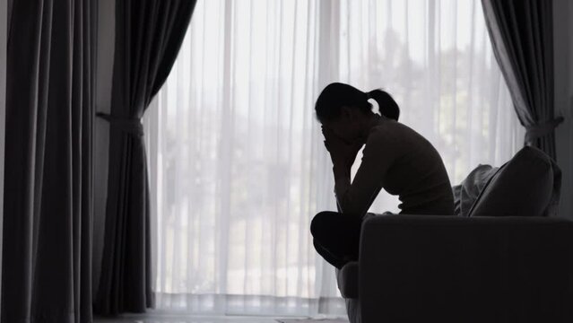 Silhouette of a person suffering from depression in the house, Depressed woman sitting alone on the Sofa feel stress, sad and worried in the dark room. person are stressed.