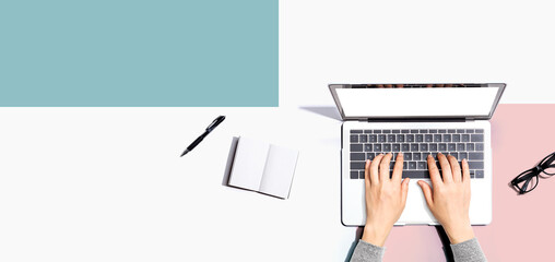 Person using a laptop computer with a notebook and eyeglasses - Flat lay - 731566615