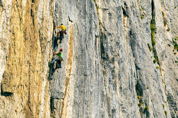 A landscape with climbers on the rock. Climber with full equipment, helmets, and glasses. Very strong textures of rock, and sunny weather. They wear helmets and sunglasses.