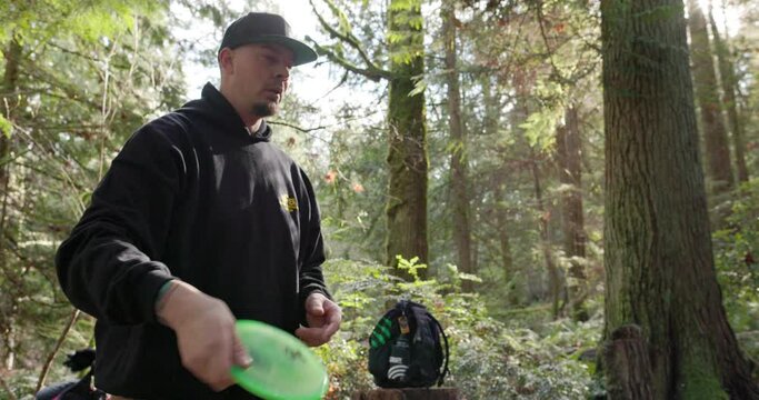 Medium shot of a man throwing a disc in the Pacific Northwest forest while playing disc golf 