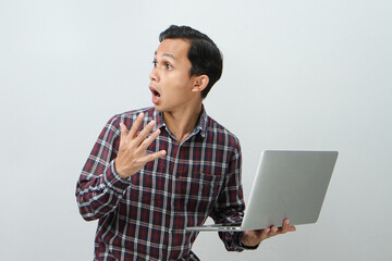 Shocked and wow expression of asian indonesian man holding laptop computer on isolated background