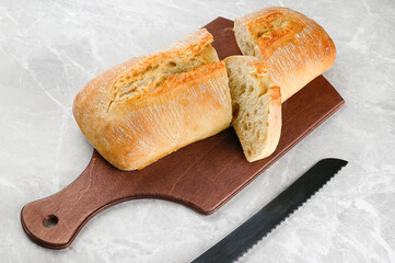 Ciabatta rustic bread beautifully cut on a cutting board with a bread knife on a light stone...