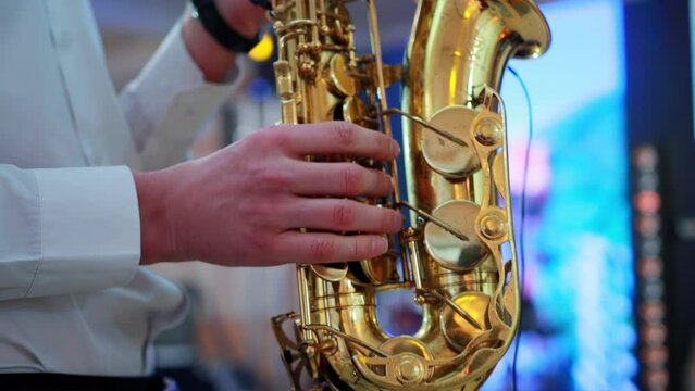 A male saxophonist plays music at an indoor concert at a festival with light and music. A golden saxophone is in the hands of a man. Slow mo