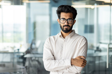 Fototapeta premium A man with a beard and glasses is standing in an office with his arms crossed