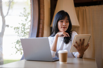 Cheerful young woman with a laptop and notebook, enjoying her work from home setup in a sunny room..