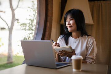 Cheerful young woman with a laptop and notebook, enjoying her work from home setup in a sunny room..