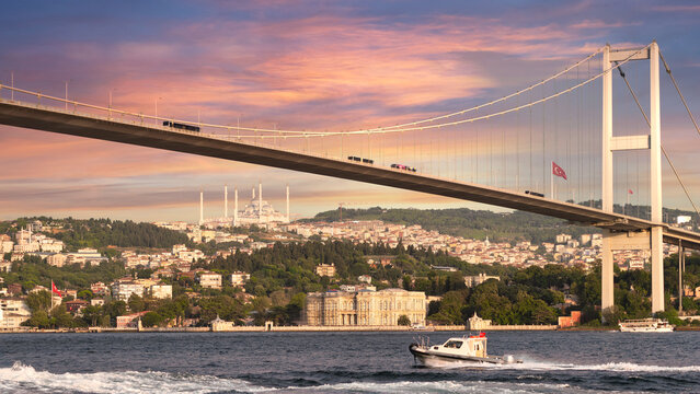 A sailboat traverses the Bosphorus Strait beneath the iconic Bosphorus Bridge, bathed in the warm glow of the setting sun