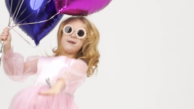 Cute girl dancing on a white background with balloons. The concept of children's theater productions and developing acting circles and children's parties.