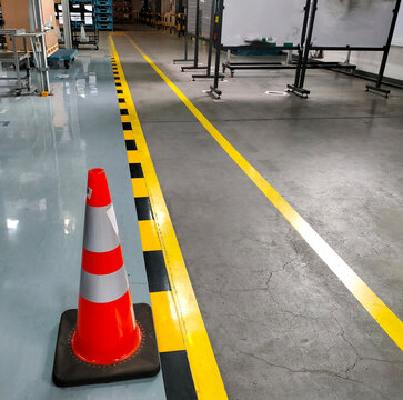 Industrial building corridor painted yellow between parallel yellow lines on abstract cement background. There are red cones located to ensure safety in pedestrian traffic.