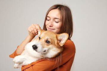 girl holding a corgi dog in her arms on a clean light background, love for dogs