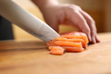 Red fish is cut into pieces with a knife on the board.