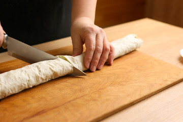 A pita roll is cut with a knife on a cutting board. Lavash dish.