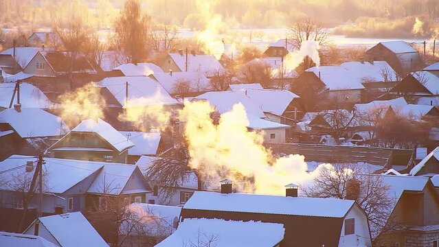 Snow-covered village houses with orange smoke coming from their chimneys against the backdrop of the sun on a frosty winter morning. Beautiful winter nature. Time lapse, village houses