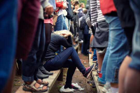 Woman, sad and alone in crowd while sitting outside at festival, protest or concert in Poland. Female supporter, exhausted or overwhelmed during outdoor fundraising event during spring or autumn