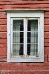 An old wooden white framed window on a weathered red painted wall.