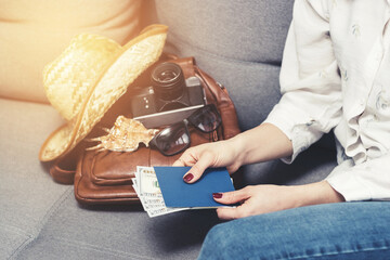 Woman holding passport and dollars cash currency, packing leather backpack with retro camera, straw...