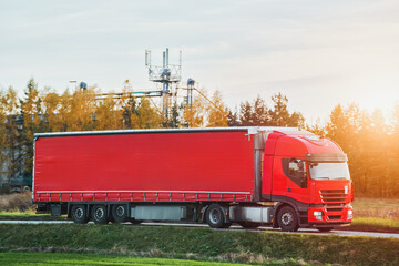 A red truck transports goods across a picturesque landscape illuminated by the golden hue of the setting sun. Truck transportation.