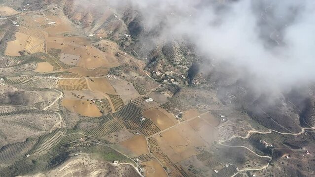 aerial view of a rural landscape with fields, patches of trees, and winding roads. Some areas are covered by clouds.