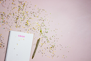 To do list concept with a white notebook, golden pen and glitter over the pink background. 