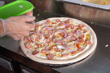 The chef prepares a classic Italian pizza with sausages, mushrooms and tomatoes.