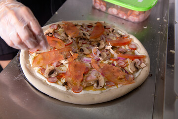 The chef prepares a classic Italian pizza with sausages, mushrooms and tomatoes.