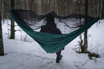 A girl sits on a hammock in the forest in winter, view from the back.
