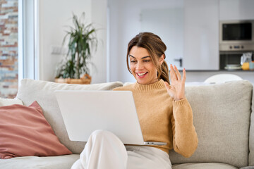 Happy mature older woman using laptop having video call sitting on couch at home. Smiling middle aged woman waving hand looking at computer chatting online relaxing on sofa in living room.