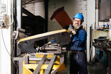 Smiling factory worker looking at camera while using machine in workshop